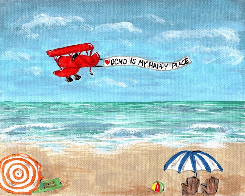 Puede incluir: Un avi&oacute;n rojo biplano vuela sobre una playa con una pancarta que dice "OCD is my happy place". La playa tiene una sombrilla a rayas azules y blancas y una pelota de playa.