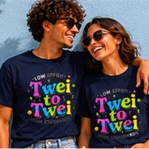 Könnte beinhalten: Ein kurzärmeliges, marineblaues T-Shirt mit dem Text "Low Effort" oben und "Twei to Twei" in großen, bunten, mehrfarbigen rosa, gelben und blauen Buchstaben, verziert mit kleinen Punkten und dem Schriftzug "High Frequency" am unteren Rand.