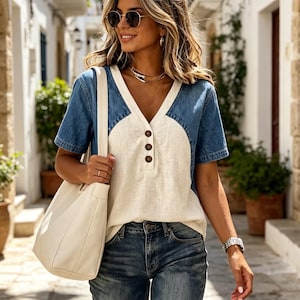 Könnte beinhalten: Ein kurzärmeliges Oberteil mit einem cremefarbenen Mittelteil, drei braunen Knöpfen sowie Ärmeln und Seitenteilen aus blauem Denim. Das Kleidungsstück wird mit einer blauen Jeans und einer großen, cremefarbenen Umhängetasche kombiniert.