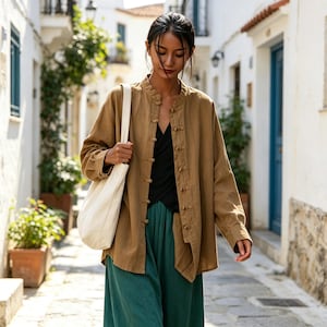 Può includere: Una camicia a maniche lunghe color marrone chiaro con colletto alla coreana e chiusure a alamaro, indossata sopra un top nero e pantaloni larghi verde scuro, con una borsa tote in tela bianca portata a spalla.
