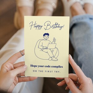 May include: A pale yellow rectangular greeting card featuring a dark blue line drawing of a person sitting in a beanbag chair using a laptop with a thumbs up. The text reads Happy Birthday! Hope your code compiles ON THE FIRST TRY.