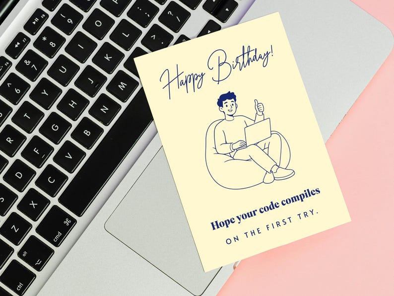 May include: A pale yellow rectangular greeting card featuring a dark blue line art illustration of a person sitting in a beanbag chair using a laptop. The text reads Happy Birthday! Hope your code compiles ON THE FIRST TRY. in dark blue ink.