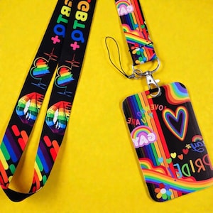 Peut inclure: Un cordon noir orné de cœurs, de lèvres aux couleurs de l'arc-en-ciel et du texte LGBTQ+ attaché à un porte-badge vertical assorti. Le porte-badge présente un motif arc-en-ciel vibrant avec des cœurs, des fleurs et le texte GAY et PRIDE.