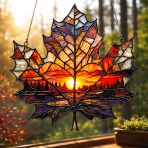 May include: A stained glass maple leaf suncatcher depicting a sunset. The leaf is crafted from orange, red, yellow, and purple glass pieces. The sunset scene features a forest silhouette and a bright sun. It hangs from a silver chain, perfect for a window display.