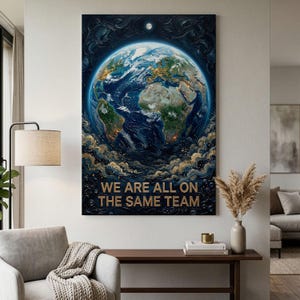 May include: A vertical wall art print featuring a textured, dark blue cosmic background with a central view of Earth. The planet displays green continents and blue oceans with golden light accents. Below the planet, the text reads WE ARE ALL ON THE SAME TEAM.