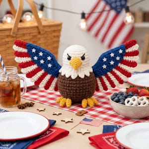 Peut inclure: Une figurine d'aigle chauve au crochet avec une tête blanche, un bec et des pattes jaunes, et un corps marron. L'aigle a de grandes ailes déployées ornées de rayures rouges, blanches et bleues avec des étoiles blanches, rappelant le drapeau américain.