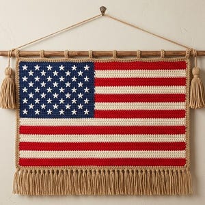 May include: A crocheted American flag wall hanging. The flag features a blue field with white stars, red and white stripes, and a fringed bottom. It is mounted on a wooden dowel with tassels on each end, and is suspended by a natural fiber cord.