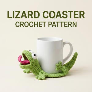 May include: A white mug is embraced by a green crochet lizard coaster with a pink tongue. The coaster has white eyes and is positioned on a light background. The text "LIZARD COASTER CROCHET PATTERN" is at the top.
