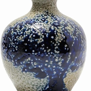 May include: A small ceramic vase with a bulbous body and a narrow neck. The surface features a textured, speckled beige finish that transitions into a deep, glossy blue glaze in the center, creating a mottled effect across the rounded exterior.