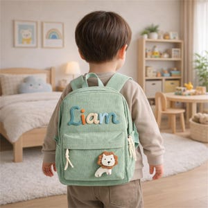 May include: A light green corduroy backpack with the name "Liam" in colorful letters. The backpack features a small lion applique and adjustable straps. This children's backpack is designed for carrying school supplies and personal items.