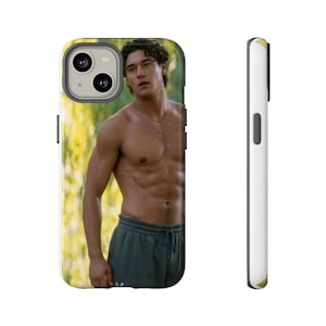 May include: White and gold phone case featuring a photograph of a shirtless person wearing green sweatpants. The phone case has a black camera lens and buttons. The side of the phone case is white.