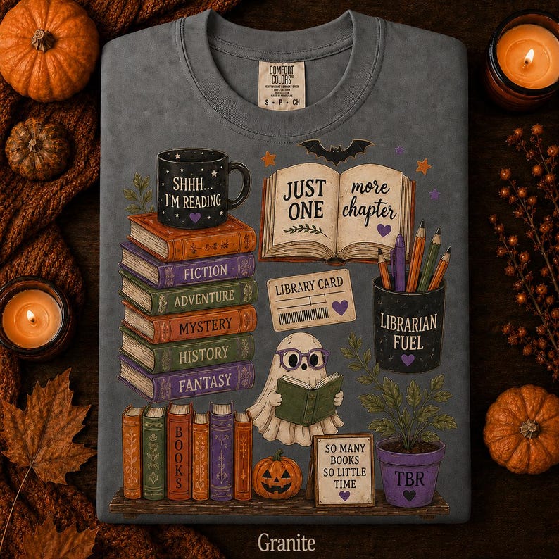 May include: A granite-colored t-shirt featuring a graphic print of a stack of books labeled Fiction, Adventure, Mystery, History, and Fantasy. The design includes a ghost reading a book, a mug reading Shhh... I'm Reading, and a pencil holder labeled Librarian Fuel.