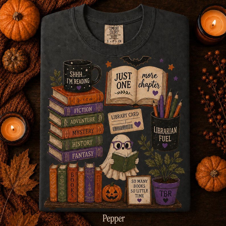 May include: A dark gray crewneck t-shirt featuring a graphic print of stacked books labeled Fiction, Adventure, Mystery, History, and Fantasy. The design includes a ghost reading a book, a mug reading Shhh... I'm Reading, and text reading Just One More Chapter, Library Card, Librarian Fuel, and So Many Books So Little Time.