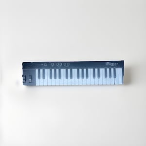 以下が含まれることがあります： 37鍵の白黒iRig:37 MIDIキーボード。キーボードの左側には一連のボタンとスイッチがあります。キーは白と黒です。「iRig:37」の文字が右側に印刷されています。