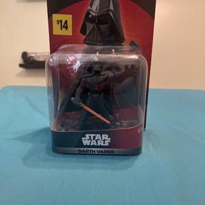 May include: A Darth Vader action figure from Star Wars, packaged in a clear plastic case. The packaging includes the Disney Infinity logo and the text "Edition 3.0". The figure is black and has a lightsaber.