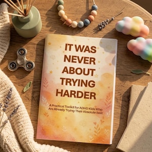 Peut inclure: Un livre intitulé « IT WAS NEVER ABOUT TRYING HARDER » avec un sous-titre sur le TDAH. L'image montre également un diffuseur vert, un collier de perles, un fidget spinner et des nuages décoratifs sur une table en bois.