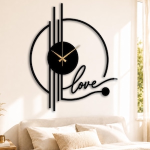 May include: Black wall clock with gold hands, featuring a circular design with vertical lines and the word "love" in cursive. The clock is mounted on a white wall above a bed.