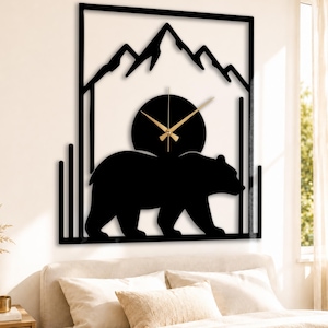Puede incluir: Reloj de pared de metal negro con silueta de oso, montañas y esfera circular. Las manecillas del reloj son doradas. El diseño está enmarcado dentro de un borde rectangular. Una pieza decorativa para una habitación con temática de la naturaleza.