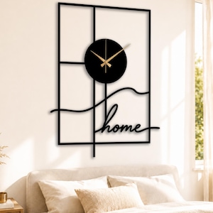Puede incluir: Reloj de pared de metal negro con marco rectangular y esfera circular. Las manecillas del reloj son doradas. La palabra "home" está escrita en cursiva debajo. El reloj está montado en una pared blanca.
