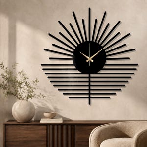 May include: A black wall clock with a sunburst design. The clock face is a black circle with gold-colored hands. The sunburst design features black lines radiating outwards and horizontally. The clock is mounted on a beige wall.