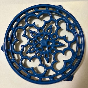 May include: A circular blue trivet featuring an intricate, openwork lattice design with a central floral-inspired motif. The metal object has a glossy finish and is constructed with a repeating pattern of curved, interconnected segments.