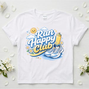 Peut inclure: T-shirt blanc avec un motif coloré « Run Happy Club ». Le motif comprend un soleil souriant, des nuages, des marguerites, une gourde et des chaussures de course. Le t-shirt est de style col rond.
