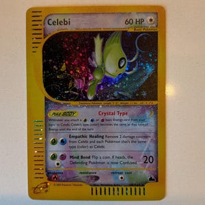May include: A Celebi trading card with 60 HP, featuring a holographic illustration of the green creature against a dark, starry background. The card has a yellow border, purple text boxes, and includes the text Crystal Type, Empathic Healing, and Mind Bend.