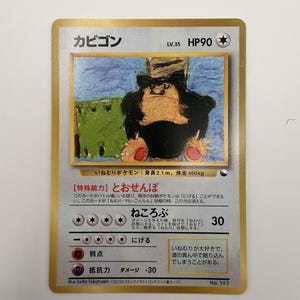 Puede incluir: Una carta coleccionable japonesa de Snorlax con borde dorado, que presenta una ilustración dibujada a mano del personaje. La carta muestra 90 HP, nivel 35, e incluye texto en japonés, con debilidad de tipo lucha y resistencia de tipo psíquico.