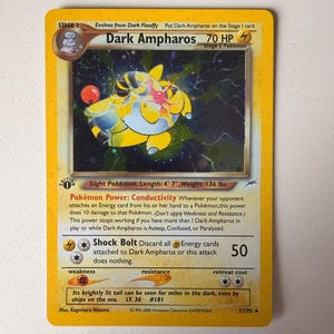 May include: A Dark Ampharos trading card with a yellow border, featuring a holographic illustration of the yellow and black creature. The card displays 70 HP, the Conductivity Pokémon Power, and the Shock Bolt attack, with 1st Edition stamp.