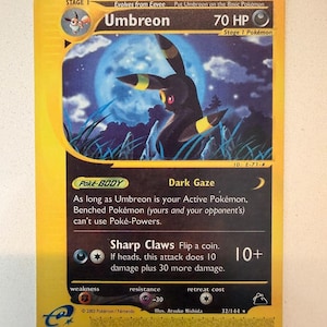 May include: A 2003 Umbreon trading card with 70 HP, featuring a dark creature with yellow rings under a full moon. The card text includes Dark Gaze and Sharp Claws attacks, with a yellow border and black background details from the Nintendo series.