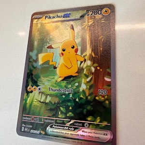 May include: A Pikachu ex trading card featuring a yellow character standing in a forest setting. The card displays 200 HP, a Thunderbolt attack with 120 damage, and the text Pokémon ex rule is Knocked Out, your opponent takes 2 Prize cards.
