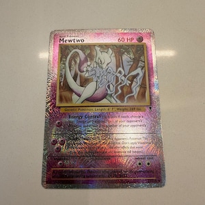 Puede incluir: Una carta coleccionable holográfica de Mewtwo con 60 HP, que muestra al personaje en un entorno forestal. La carta muestra el texto Energy Control y Telekinesis, junto con la descripción del Pokémon Genético, su altura de 201 cm y peso de 122 kg.