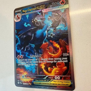 May include: A Mega Charizard X ex trading card featuring a holographic illustration of a large black dragon with blue flames, alongside smaller orange dragon-like creatures. The card displays 360 HP, the Inferno X attack, and the text 125/094.