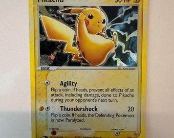 Può includere: Una carta collezionabile di Pikachu con 50 HP e un simbolo di energia elettrica. La carta presenta un'illustrazione olografica di Pikachu, gli attacchi Agility e Thundershock, e testo che include 2003 Pokemon/Nintendo, 012 e 003-ZA5-3JL.
