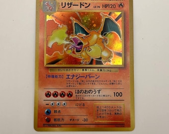Può includere: Una carta collezionabile giapponese Charizard con un'illustrazione olografica della creatura arancione simile a un drago che sputa fuoco. La carta mostra il nome リザードン, HP120 e varie statistiche di gioco, tra cui la potenza d'attacco e i requisiti energetici stampati in giapponese su uno sfondo arancione ardente.
