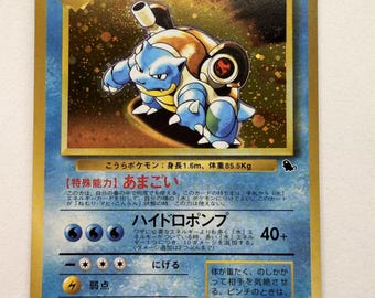 以下が含まれることがあります： 金色の縁取りが施されたカメックスの日本語版トレーディングカード。背中に大砲を背負った青い水タイプのポケモンが描かれている。カードにはHP100、名前、特殊能力、ハイドロポンプの技に関する日本語のテキストが記載されている。