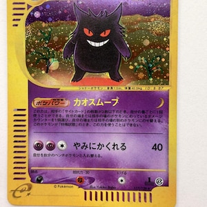 Puede incluir: Una carta coleccionable Pokémon de Gengar en japonés que muestra un personaje de tipo fantasma morado con ojos rojos y una amplia sonrisa. La carta tiene un borde dorado, fondo holográfico, 90 HP, texto en japonés y el logo de Pokémon.