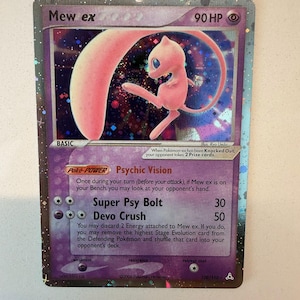 May include: A Mew ex trading card featuring a holographic purple background and a pink Mew character illustration. The card displays 90 HP, the Psychic Vision Poke-Power, and attacks Super Psy Bolt and Devo Crush, with text detailing game mechanics.