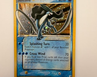 Può includere: Una carta collezionabile Pokémon Suicune Gold Star con 80 HP. La carta presenta un'illustrazione olografica del personaggio Suicune blu e nero, con gli attacchi Splashing Turn e Cross Wind elencati sotto. Il bordo è di colore giallo.