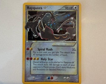Può includere: Una carta collezionabile Rayquaza con 90 HP, che mostra l'illustrazione di una creatura nera simile a un drago. La carta presenta gli attacchi Spiral Rush e Holy Star, con bordi gialli e sfondo grigio argento, contrassegnata 107/107 del 2005.