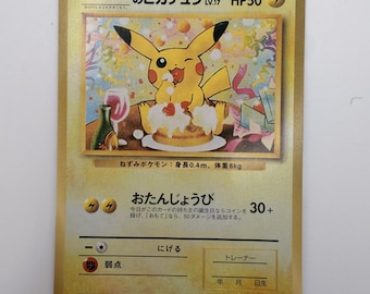 Può includere: Una carta collezionabile giapponese di Pikachu con bordo dorato che raffigura un personaggio giallo che mangia una torta con un bicchiere di vino e coriandoli sullo sfondo. La carta mostra HP50, il testo Otanjo-bi e uno spazio per la data.