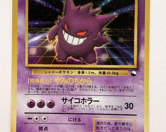 Può includere: Una carta collezionabile di Gengar raffigurante una creatura viola con occhi rossi e un ampio sorriso. La carta presenta un bordo dorato, uno sfondo viola con un motivo a griglia e testo in giapponese, inclusi HP80, livello 40 e statistiche di gioco.