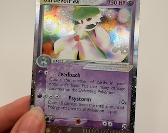 Può includere: Una carta collezionabile olografica Gardevoir ex con 150 HP, caratterizzata da uno sfondo viola e dagli attacchi Feedback e Psystorm. La carta mostra l'illustrazione del personaggio, lo stadio di evoluzione 2 e il testo del gioco.