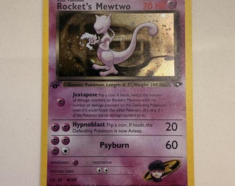 Può includere: Una carta collezionabile Rocket's Mewtwo con bordo viola e cornice gialla. La carta presenta il personaggio Mewtwo, 70 HP e gli attacchi Juxtapose, Hypnoblast e Psyburn. Include il logo del Team Rocket, il timbro 1st Edition e del testo.