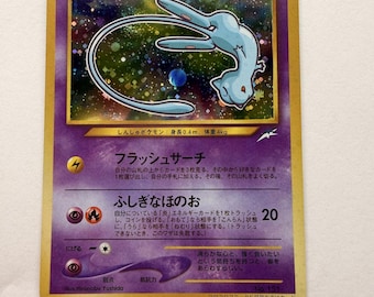 Può includere: Una carta collezionabile Pokémon Shining Mew giapponese con bordo viola e dettagli in lamina d'oro. La carta presenta un'illustrazione olografica del personaggio Mew azzurro, HP50, e testo in giapponese, incluso il nome Hikaru Mew.
