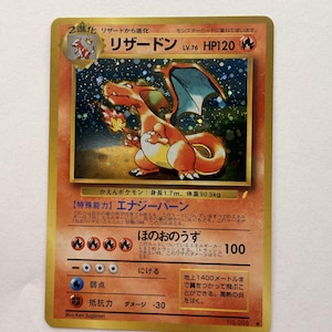 Könnte beinhalten: Eine japanische Glurak-Sammelkarte mit einer holografischen Illustration des orangefarbenen, drachenähnlichen Wesens mit blauen Flügeln. Die Karte zeigt den Namen, 120 KP, Feuer-Energiesymbole und japanischen Text zu Fähigkeiten und Angriffen.