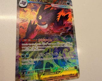 Può includere: Una carta collezionabile giapponese Mega Gengar ex con un'illustrazione olografica di una creatura viola di tipo spettro con un occhio giallo. La carta mostra 350 HP, testo in giapponese e il numero di set 240/193 SAR su uno sfondo colorato e ardente.