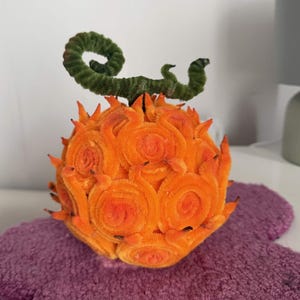 May include: A spherical orange object crafted from pipe cleaners, featuring a textured surface with swirling patterns and pointed protrusions. A green, coiled stem made of pipe cleaners extends from the top of the orange, textured, fruit-like structure.