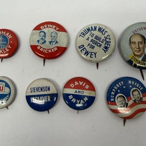 May include: A collection of eight round political campaign buttons featuring various designs, including portraits of candidates, text such as Truman, Barkley, Dewey, Bricker, LBJ, Stevenson, Kefauver, Davis, Bryan, Humphrey, and Muskie, and patriotic color schemes.