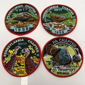 May include: Four circular embroidered patches featuring wild turkeys. Each patch displays the text Pennsylvania Chapter or PA Chapter and NWTF. The patches are dated 1998, 1999, 2000, and a 25th Anniversary 1975-2000 edition, all with red borders.